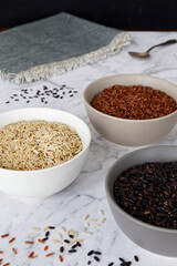 Rice of different colors: brown, red and black in a bowl. Assortment of rice grains on marble table.