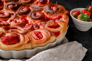 Baking dish with strawberry cinnamon rolls and napkin on dark background, closeup