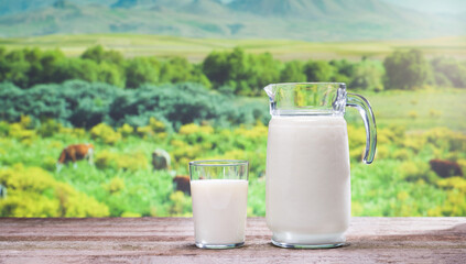 Fresh milk and spring time. Glass jug and glass of organic milk on wooden table. Cows in the meadow in the background. Healthy eating concept.