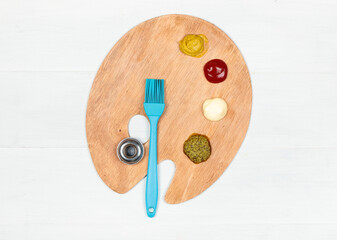 Wooden artistic palette with pressed sauces for cooking and a culinary silicone brush. Top view
