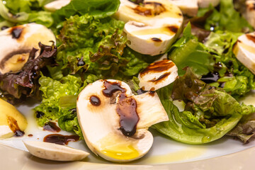 Salad with mushrooms shiitake, champignons, white , beef, arugula, cherry tomatoes and balsamic vinegar on a round white ceramic plate
