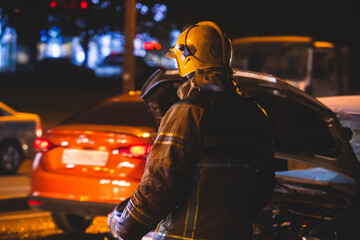 Fototapeta na wymiar Group of fire men in uniform during fire fighting operation in the night city streets, firefighters with the fire engine truck fighting vehicle in the background, emergency and rescue