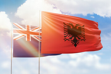 Sunny blue sky and flags of albania and new zealand