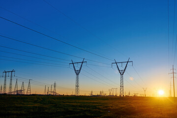 Sun rise on field with high voltage electricity towers. Dark silhouettes of repeating power lines...