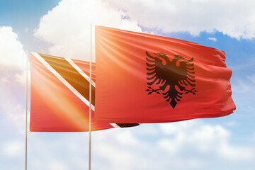 Sunny blue sky and flags of albania and trinidad and tobago
