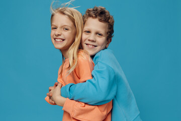 beautiful, happy children stand on a blue background in bright sweatshirts and hug each other...