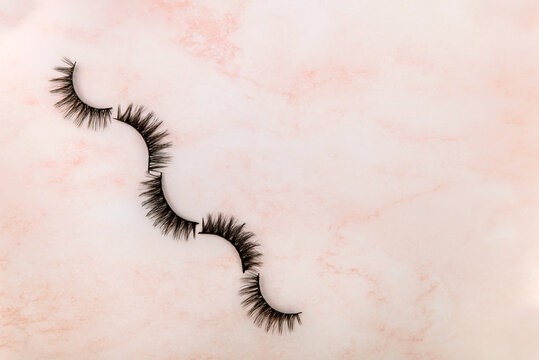 Set of false artificial eyelashes on the top of rose background. Eyelash extension tools. Flat lay, Top view