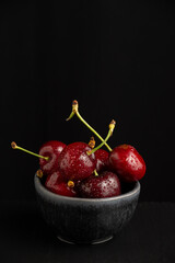 Top view of cherries with water drops in black bowl, selective focus, black background, vertical, with copy space