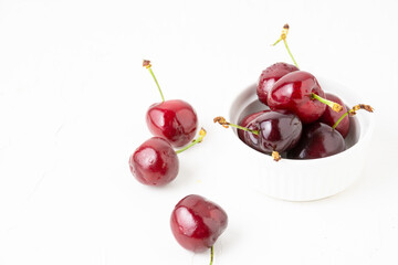 Top view of cherries in white bowl, selective focus, on white table, horizontal, with copy space