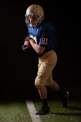 Full length view of football player running with the ball on grass field and dark background © Daniel Thornberg