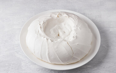 White plate with meringue for Pavlova cake on a light gray background, top view. Cooking delicious homemade dessert