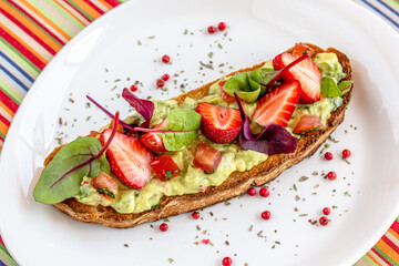 Keto diet avocado toast with strawberries, soft cheese, sesame seeds and herbs. healthy Breakfast or lunch. sandwich recipe mix media. top view, selective focus