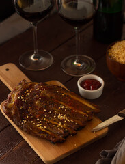 Baked ribs with seasoning on the board, two glasses of red wine.