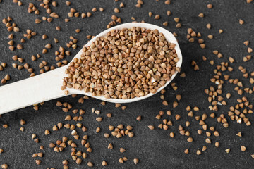 Uncooked buckwheat in a spoon on dark old boards. Buckwheat is used for cooking.