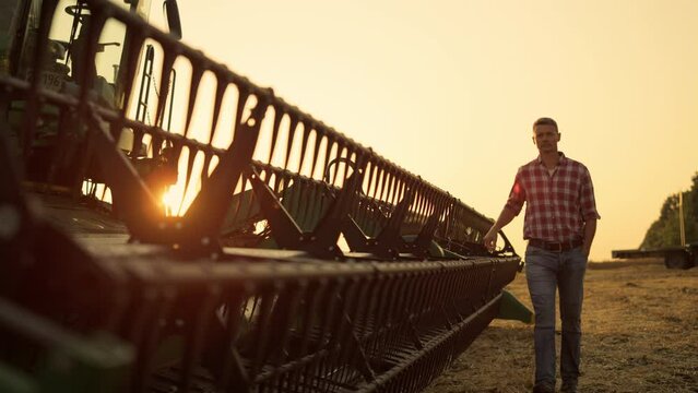 Worker inspect combine thresher countryside at golden sunset. Farming vehicle 