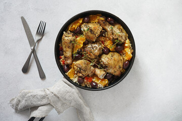 Basque chicken stew with peppers, olives, thyme and oranges close-up in a frying pan on the white table. top view