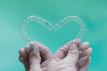 Hands holding dental aligners in heart shape on blue background