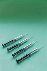 4 Full plastic syringes on tiffany blue color pastel background, with teeth whitening gel inside