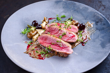 Gegrilltes Gourmet Entenbrust Filet mit Haut serviert mit Pilzen und Amarena Kirschen in Trüffel Creme als close-up auf einem Design Teller