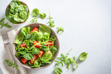Green salad with fresh leaves and tomatoes on white kitchen table. Top view, copy space.