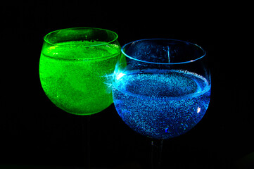 Two alcohol drinks - Blue curacao and Tokyo tea - close up photo. They are illuminated with the backlight and having black background behind. Background picture.