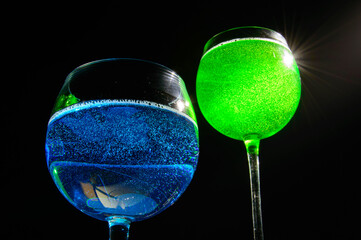 Two alcohol drinks - Blue curacao and Tokyo tea - close up photo. They are illuminated with the backlight and having black background behind. Background picture.