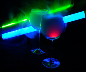 Two smoky cocktails with a neon tube and green laser, on a dark background. One of the glasses slowly igniting alcohol inside. Dangerous liquor mixture - close up photo. Background picture.