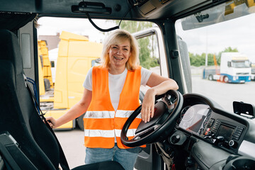 Mature woman truck driver steering wheel inside lorry cabin. Happy middle age female trucker...