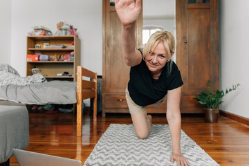 mature woman at home doing sport yoga on the floor with laptop online classes 