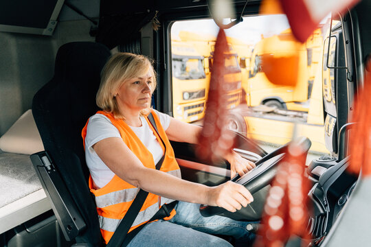 Mature Woman Truck Driver Steering Wheel Inside Lorry Cabin. Happy Middle Age Female Trucker Portrait 