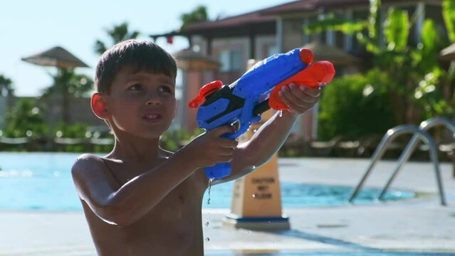 Close-up of a little boy shooting a toy water gun in a public pool