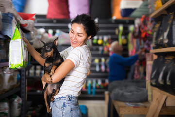 Obraz premium Happy female customer with dog choosing dry food in petshop