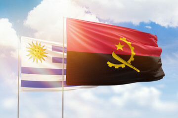 Sunny blue sky and flags of angola and uruguay