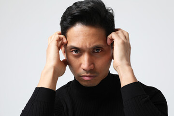 Headshot of Asian man touches his face looking at the camera. Mental health.