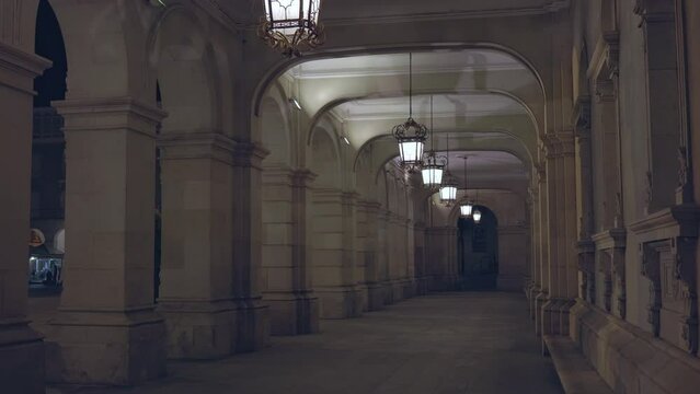 A beautiful historical corridor of collona, which is illuminated by lanterns at night. Beautiful powerful antique collones on the left side, going through the arch into the wall on the other side