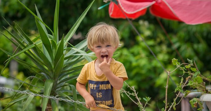 little blond baby boy points his finger to his mouth in summer garden