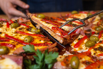 person cutting matambre to pizza with bell peppers and olives to serve