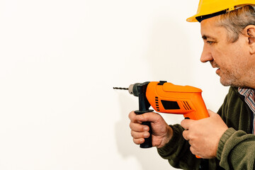 Worker drilling a hole with a drill on a white wall. Copy space.