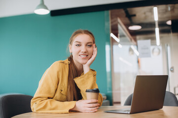 Smiling businesswoman with cup of coffee sitting at desk in office