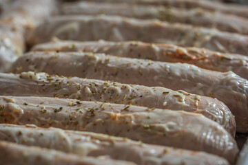 Raw seasoned sausages on baking tray closeup