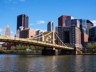 Yellow bridge and Pittsburgh downtown against blue sky.