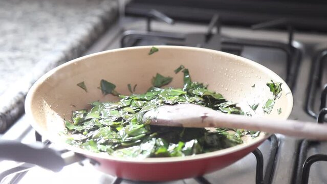 Hands cooking ora-pro-nobis (Pereskia aculeata) in a frying pan, a popular edible plant in Brazil