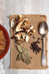Mushroom soup with dried porcini mushrooms, bay leaf and pepper on rustic table texture background.