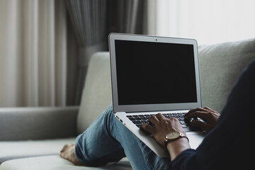 Rear view of young man freelance sitting on at home and using laptop computer to communicate with colleagues.