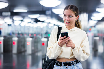 Attractive woman in blue jeans passing through ticket gates in a public transportation station