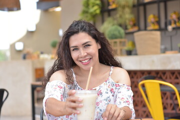 Mujer Latina sentada en restaurante cafetería contenta con bebida en mano 