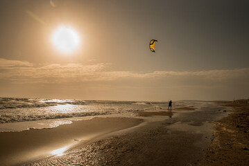 Silhouette of a kite surfer on the beach flying a kite at sunset