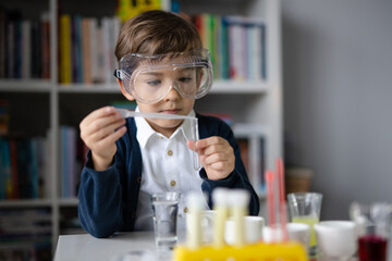 One small caucasian boy scientist five years old wearing protective eyeglasses sitting at the table playing with chemistry equipment toy preforming experiment learning and education concept front view