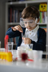 One small caucasian boy scientist five years old wearing protective eyeglasses sitting at the table...