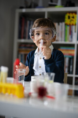 One small caucasian boy scientist five years old wearing protective eyeglasses sitting at the table playing with chemistry equipment toy preforming experiment learning and education concept front view
